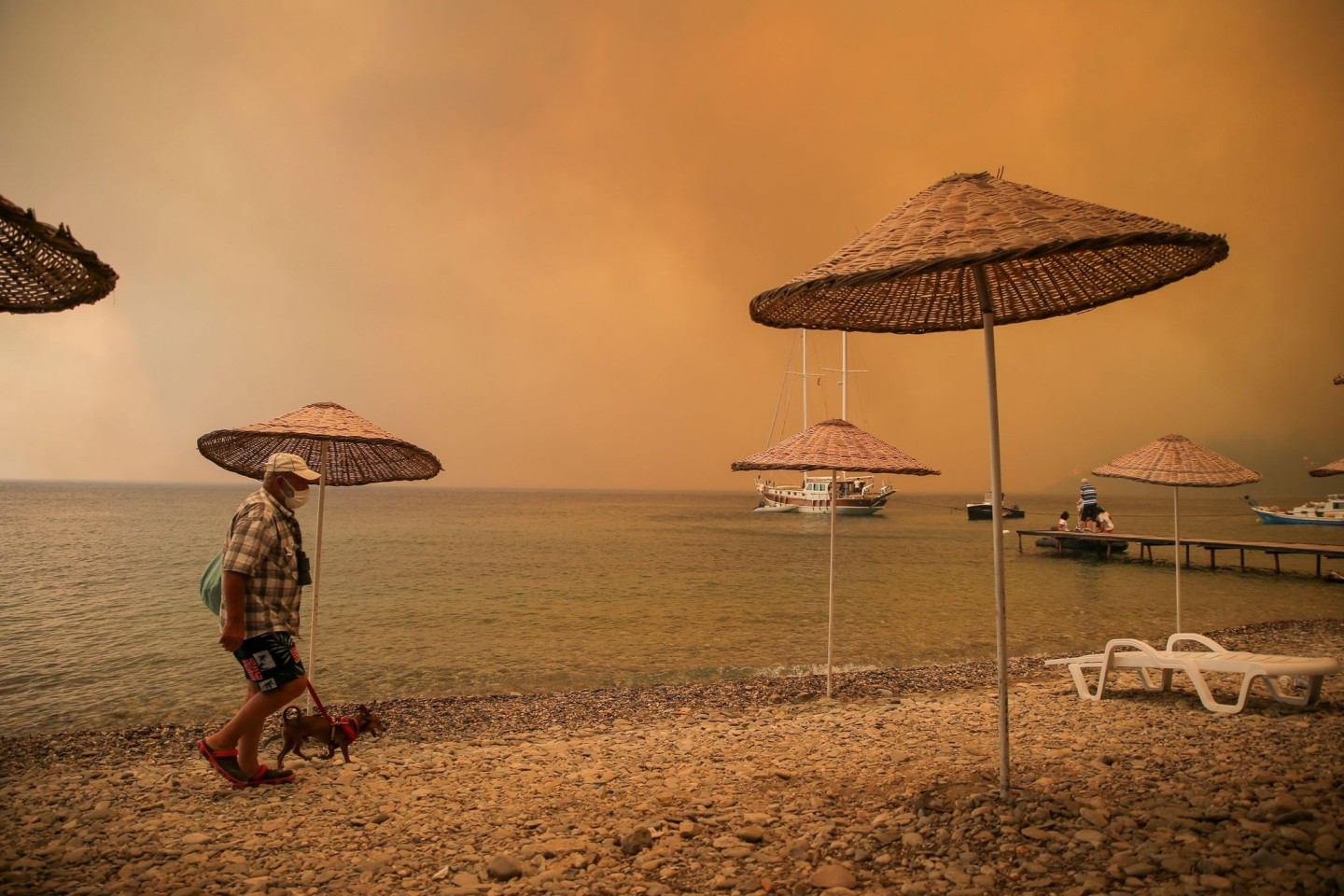 Ein Mann spaziert mit seinem Hund durch rauchverhangene Luft an einem türkischen Strand.