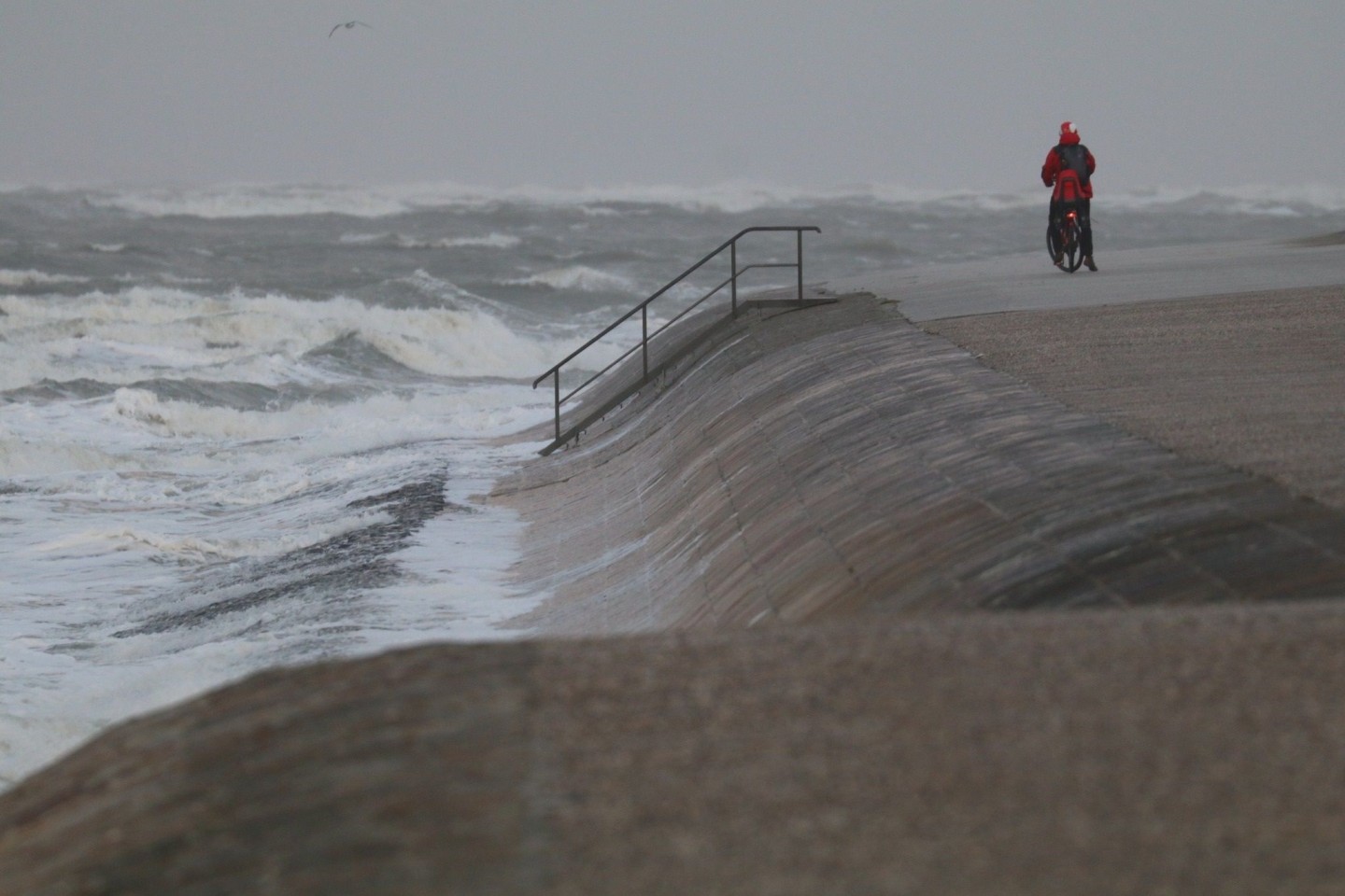 Eine Radfahrerin steht bei stürmischem Wetter an der Wasserkante auf der Insel Norderney. Ein Tiefausläufer sorgt für stürmisches Wetter im Norden.