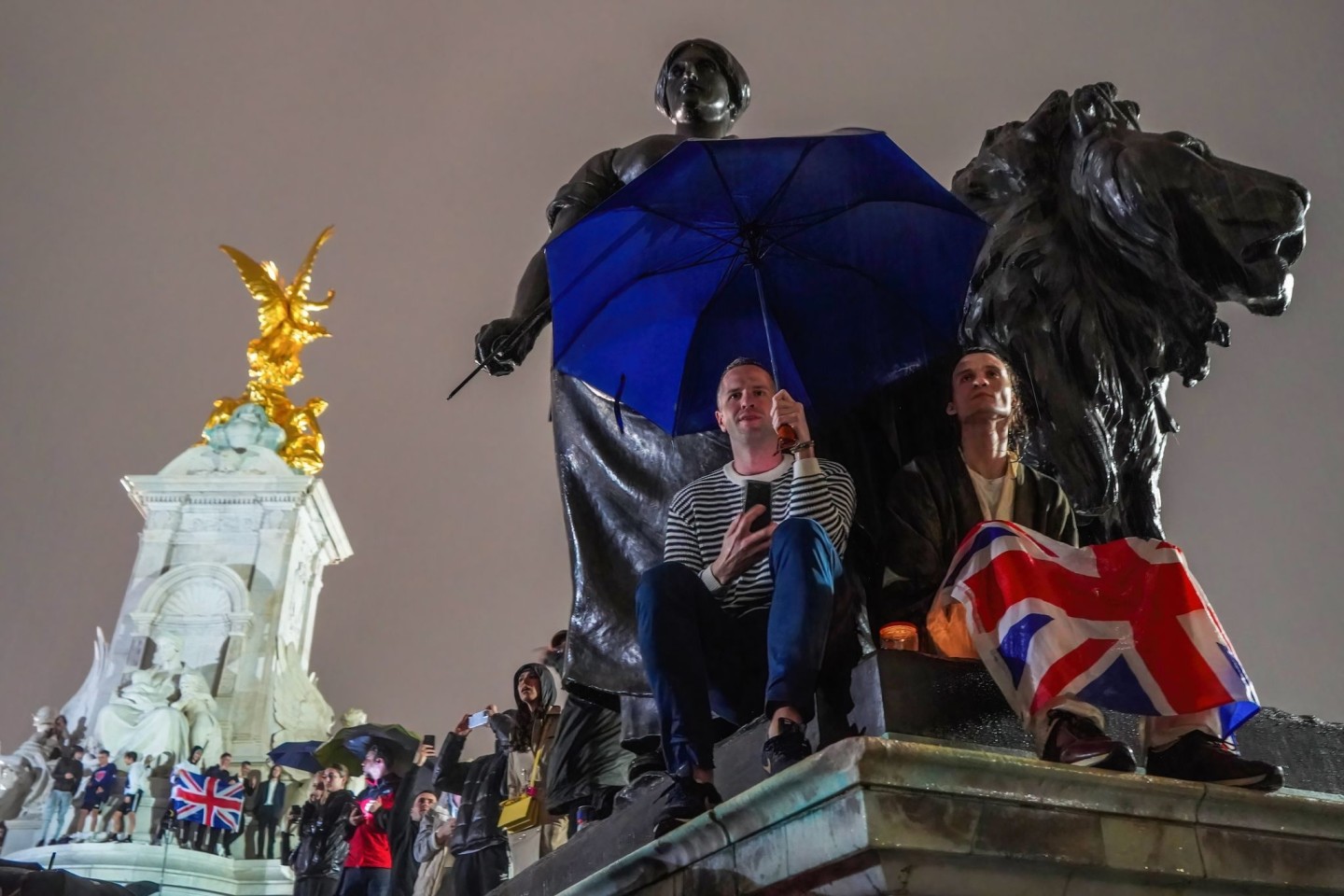 Menschen versammeln sich mit Regenschirmen und Flaggen, um Königin Elizabeth II. die letzte Ehre zu erweisen.