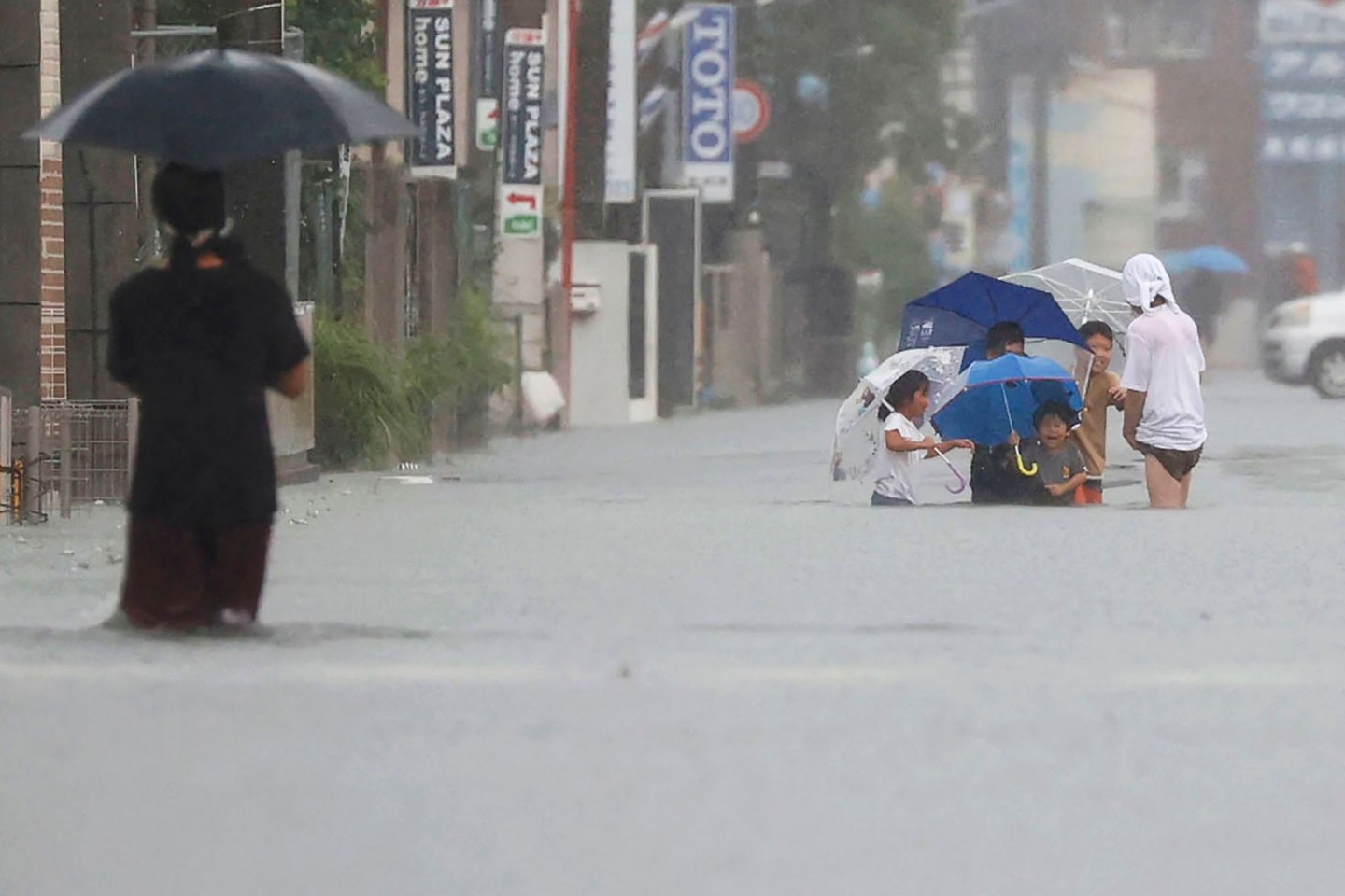 Menschen waten durch eine von starkem Regen überflutete Straße in Kurume, Präfektur Fukuoka, Westjapan.