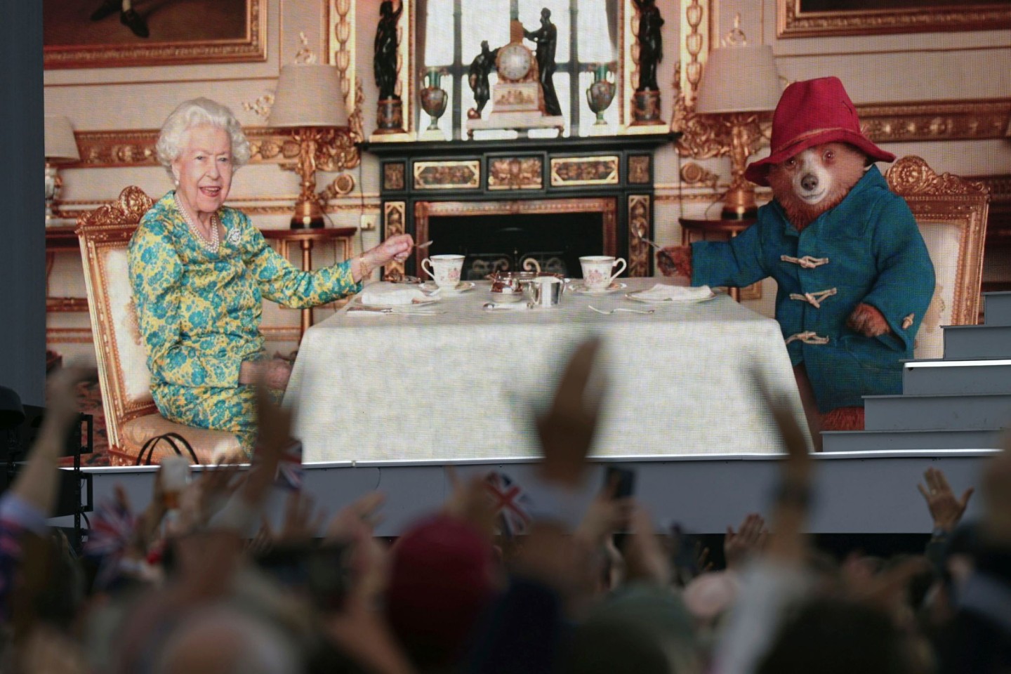 Die Zuschauer sehen auf einer großen Leinwand während der Platin-Party vor dem Buckingham-Palast Elizabeth II. beim Tee mit Paddington Bear.