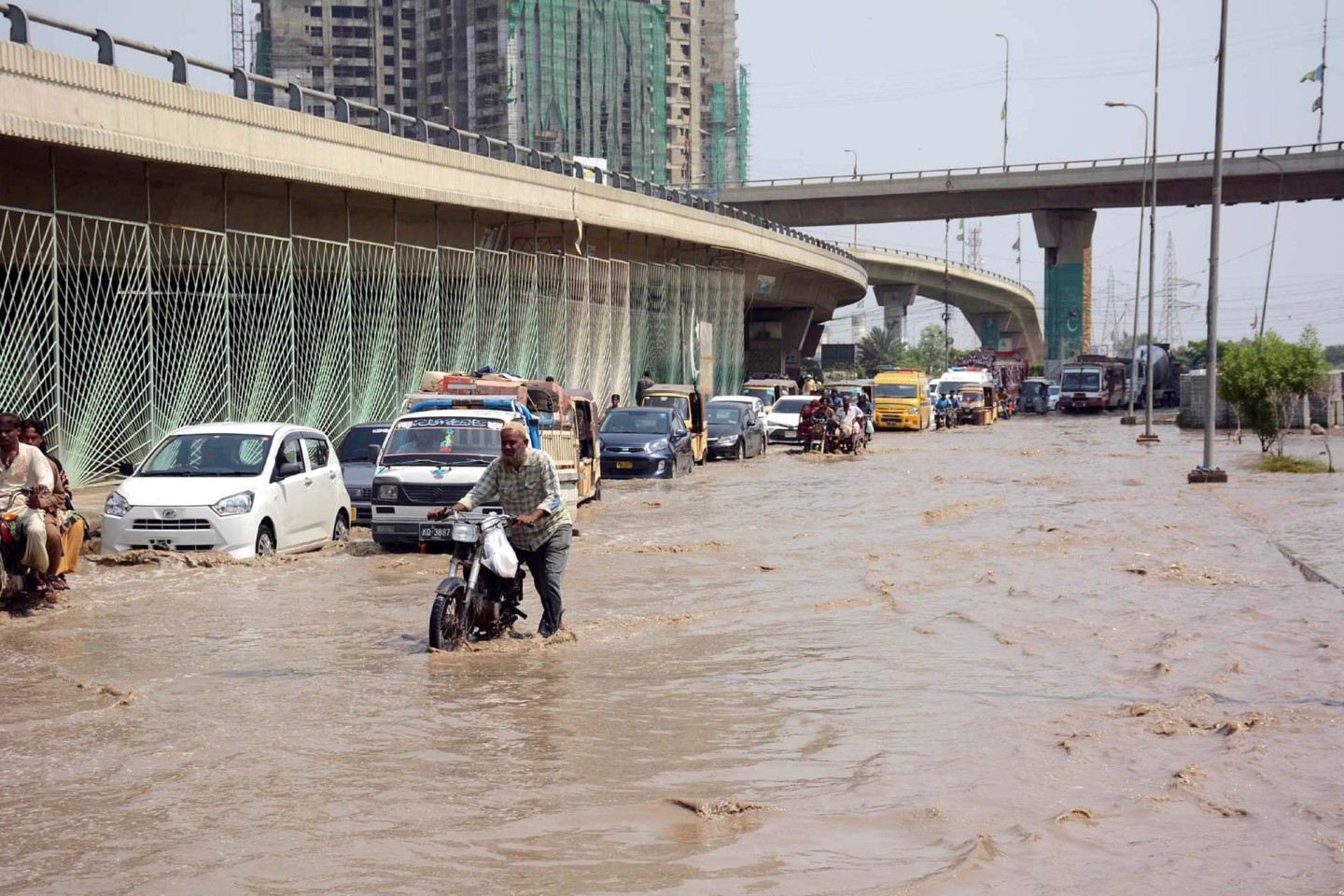 Motoradfahrer und Autos kämpfen sich durch eine überflutete Straße in Karachi.
