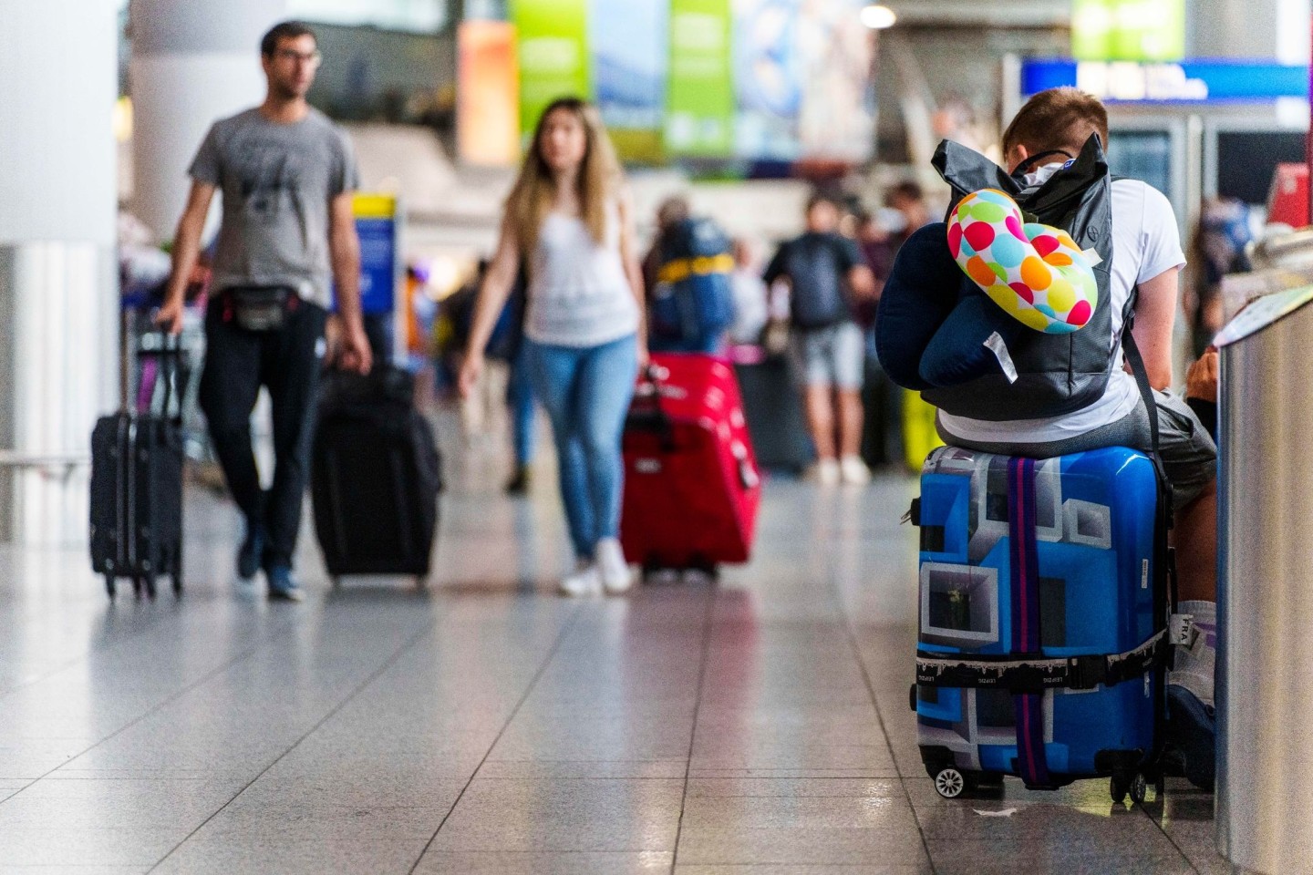 Ein junger Mann ruht sich auf seinem Koffer im Flughafen Frankfurt Main aus.