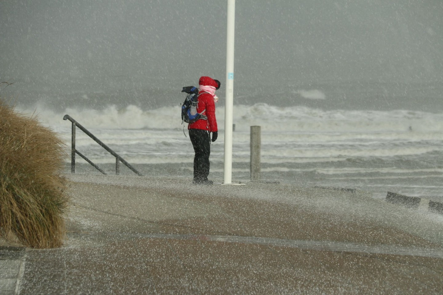 Eine Spaziergängerin blickt auf Norderney auf den Nordstrand und die Wellen der vom Sturm aufgepeitschten Nordsee, während ein Hagelschauer über sie heruntergeht.