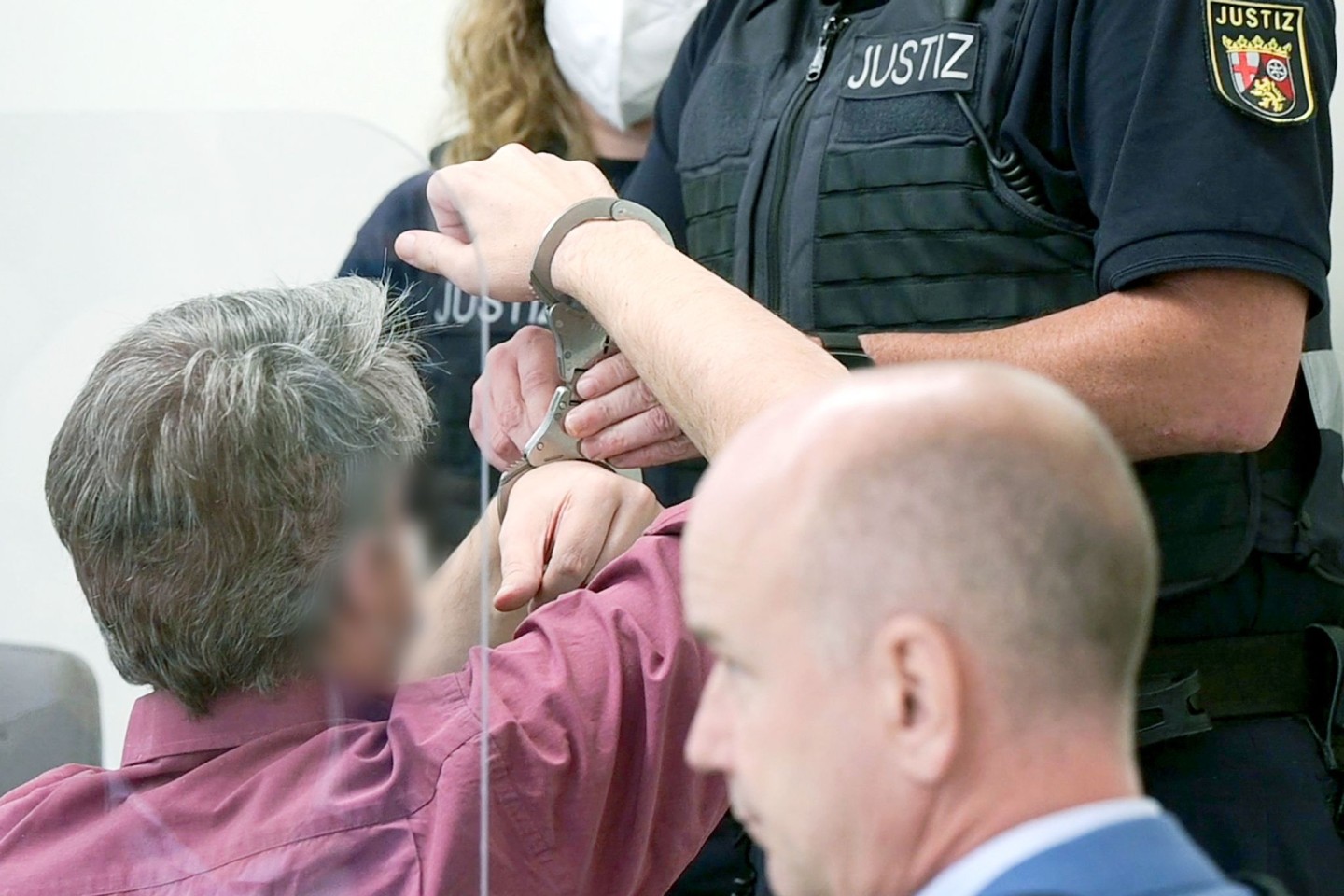 Ein Justizbeamter nimmt dem Angeklagten (l) vor dem Landgericht die Handschellen ab.