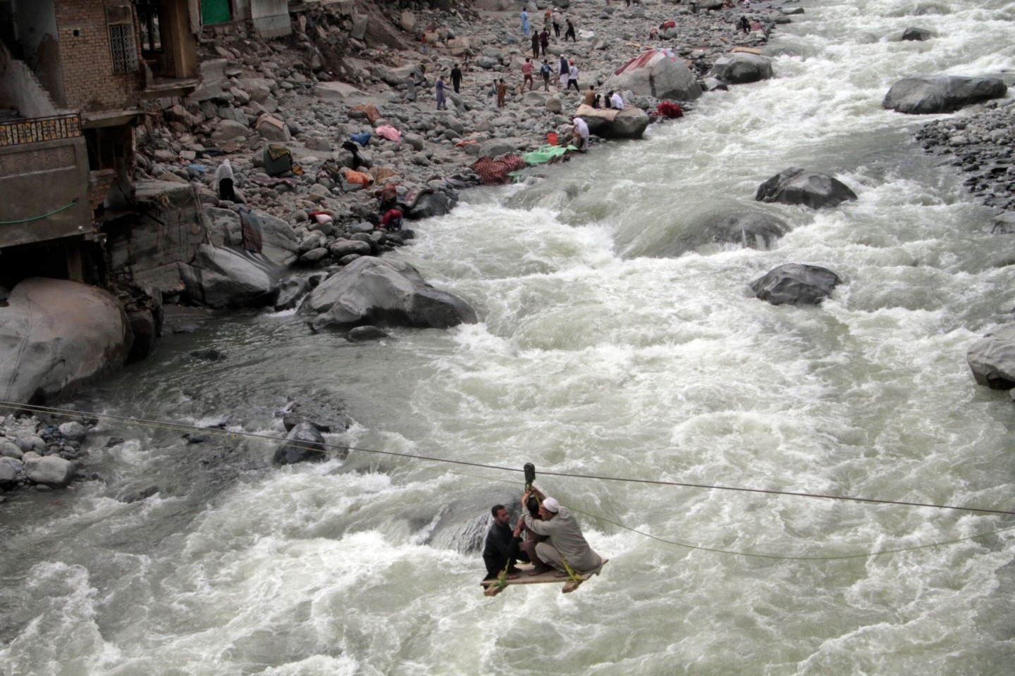 Menschen überqueren einen Fluss mithilfe einer Seilbahn.