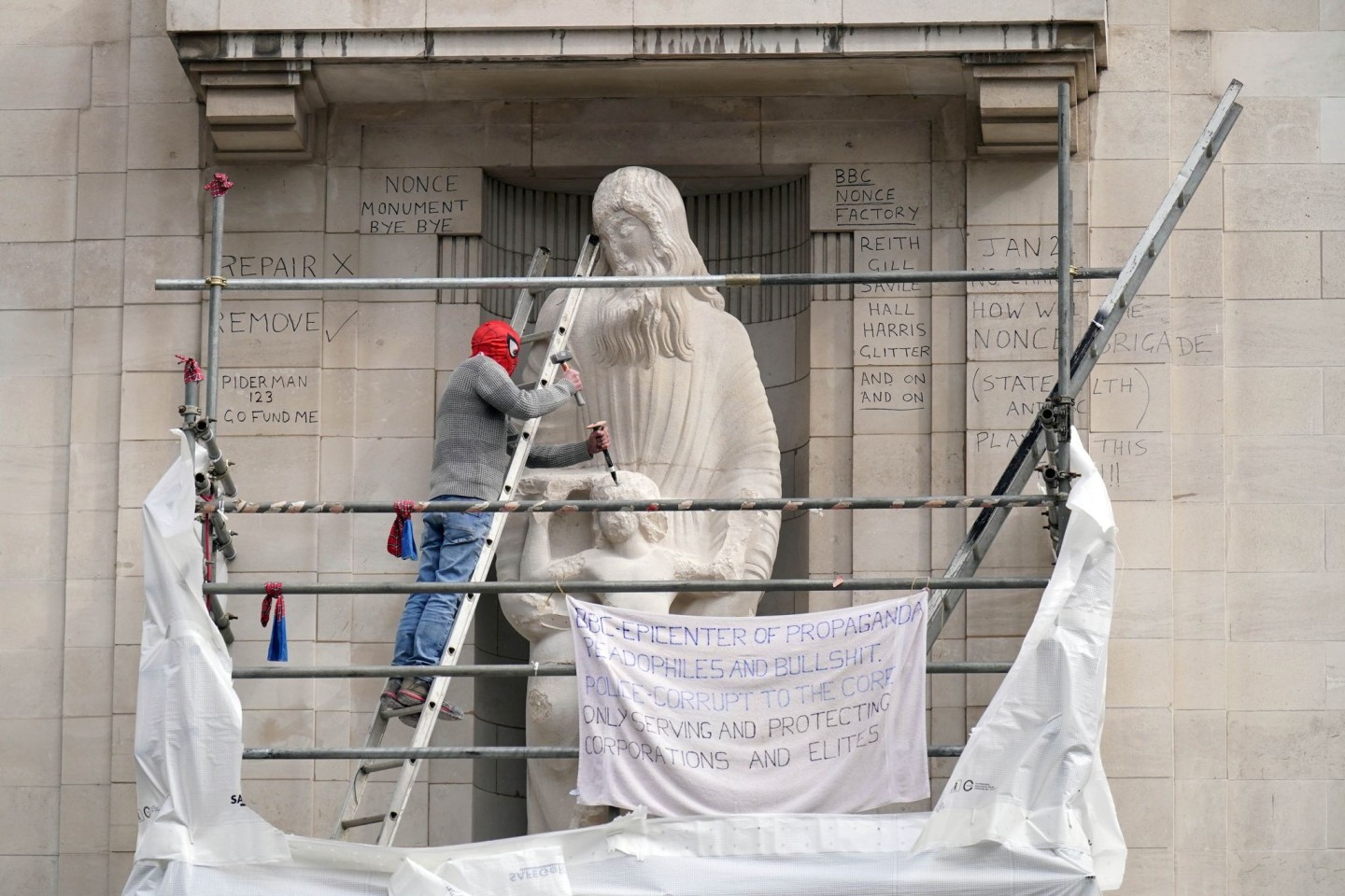 Ein Mann mit einer Spiderman-Maske beschädigt die Statue eines umstrittenen Bildhauers am Hauptquartier der BBC in London.
