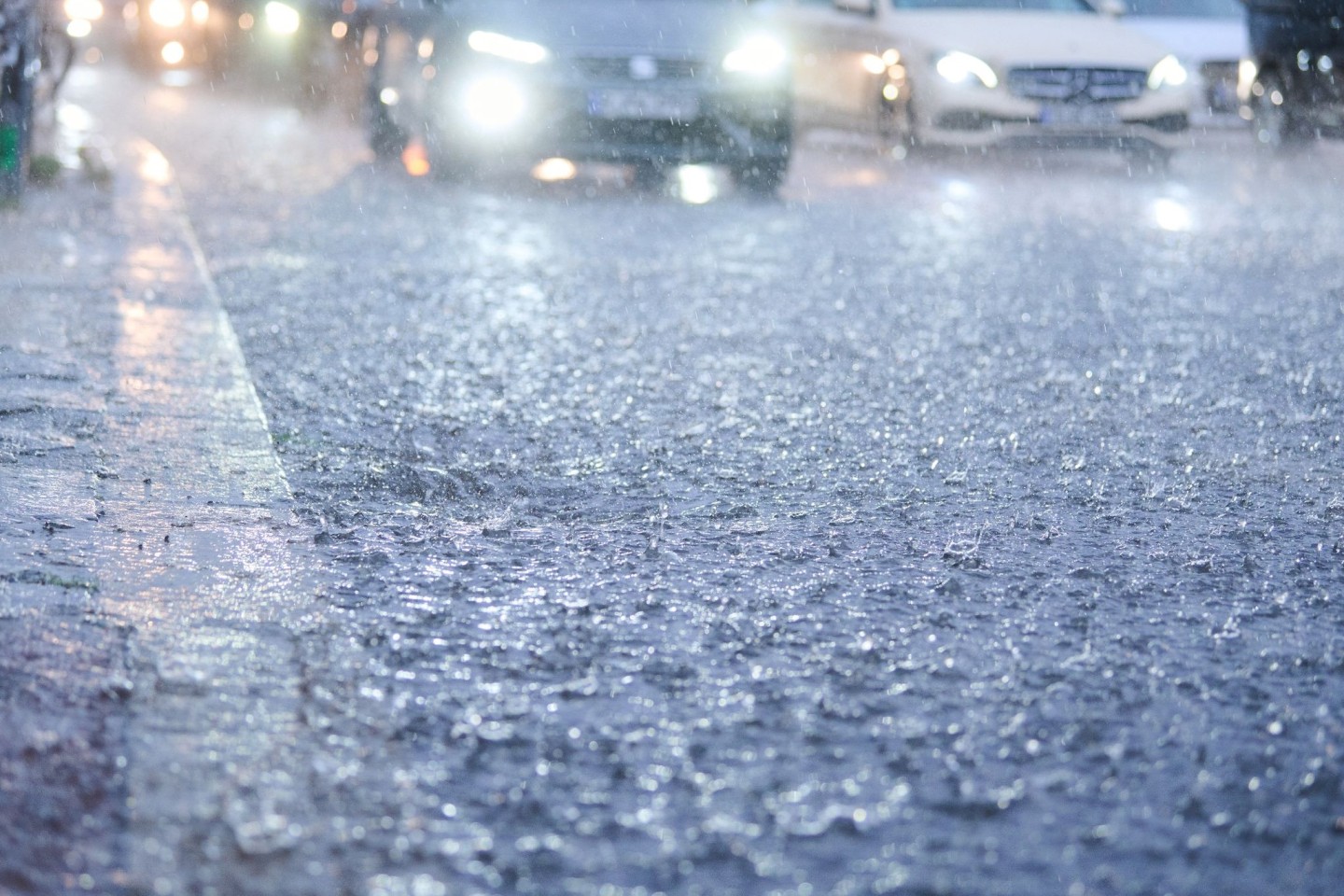 Autos fahren in Berlin bei starkem Regen durch tiefe Pfützen die sich auf der Fahrbahn gebildet haben.