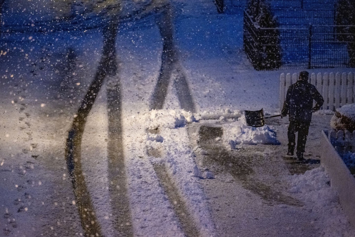Ein Mann geht am frühen Morgen mit einer Schneeschaufel auf einer zugeschneiten Straße.