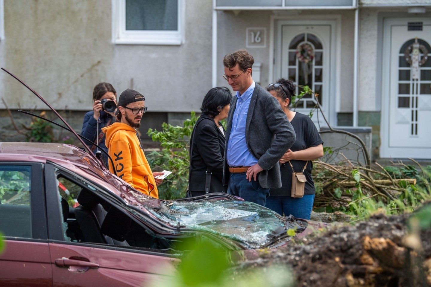 Hendrik Wüst (CDU, 2.v.r.), Ministerpräsident von Nordrhein Westfalen, spricht in Lippstadt mit einem Anwohner, dessen Auto durch den Sturm zerstört wurde.