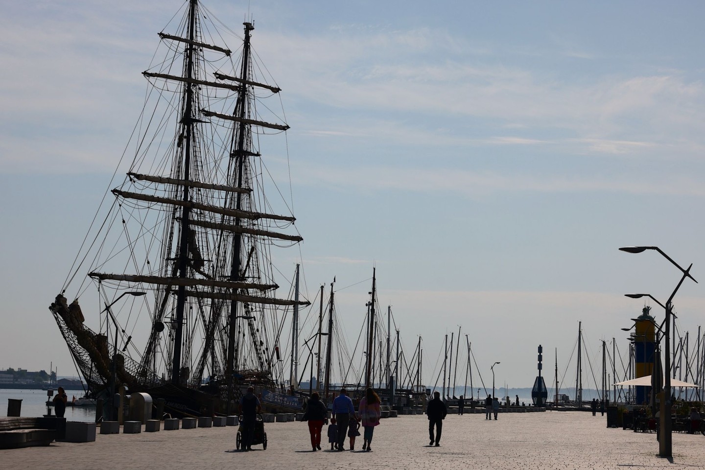 Menschen gehen bei sonnigem Wetter am Hafen von Eckernförde spazieren.
